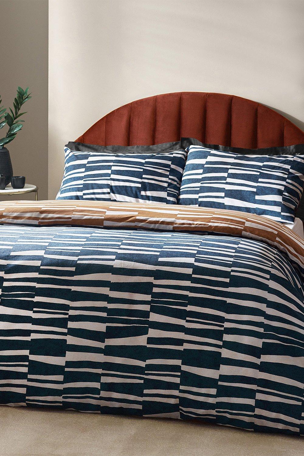 Dark blue reversible duvet cover set with abstract stripe pattern, crafted from cotton-rich material, includes matching pillowcases, displayed on a stylish bed with a curved headboard.