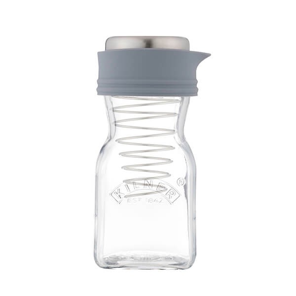 Clear glass dressing maker with a spiral whisk inside, topped with a gray silicone lid and stainless steel cap, featuring the Kilner logo embossed on the front.