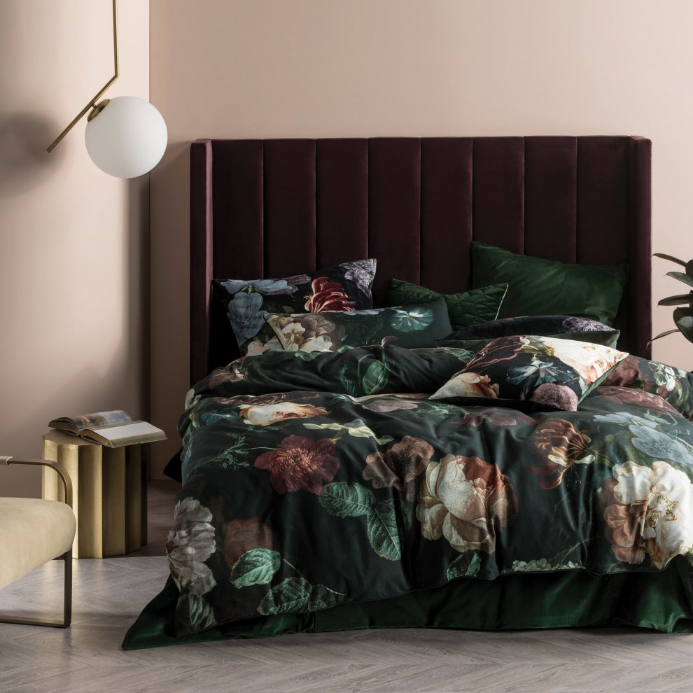 Linen House Winona Duvet Set in Ivy features a dark green floral design on soft cotton, complemented by decorative pillows and a plush burgundy headboard in a stylish bedroom setting.
