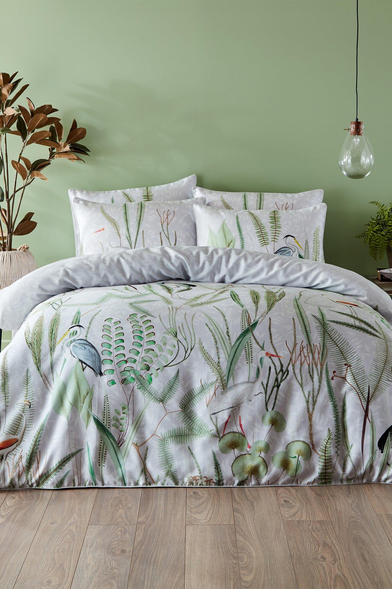 Cotton double duvet cover set featuring a vibrant multi-colored botanical print with birds and greenery, complemented by matching pillowcases, set against a soft green wall.