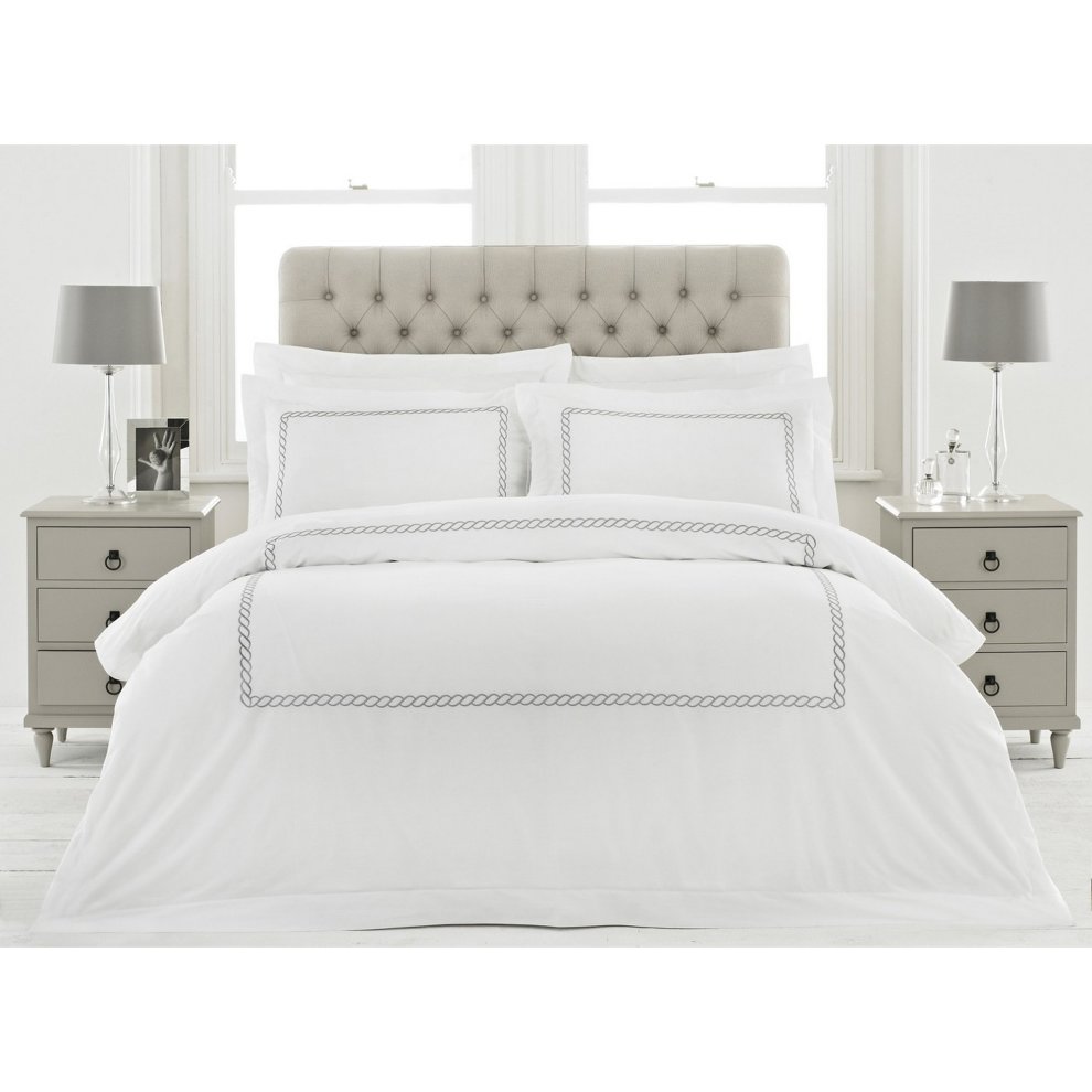 White cotton duvet cover set featuring a silver rope border, complemented by matching pillowcases, styled on a tufted headboard with grey nightstands and lamps.