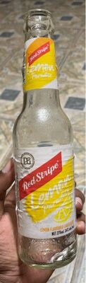 Clear glass bottle of Red Stripe Lemon Paradise Premium Lager, featuring a yellow and red label with lemon graphics, held in a hand, with a textured surface and a twist-off cap.