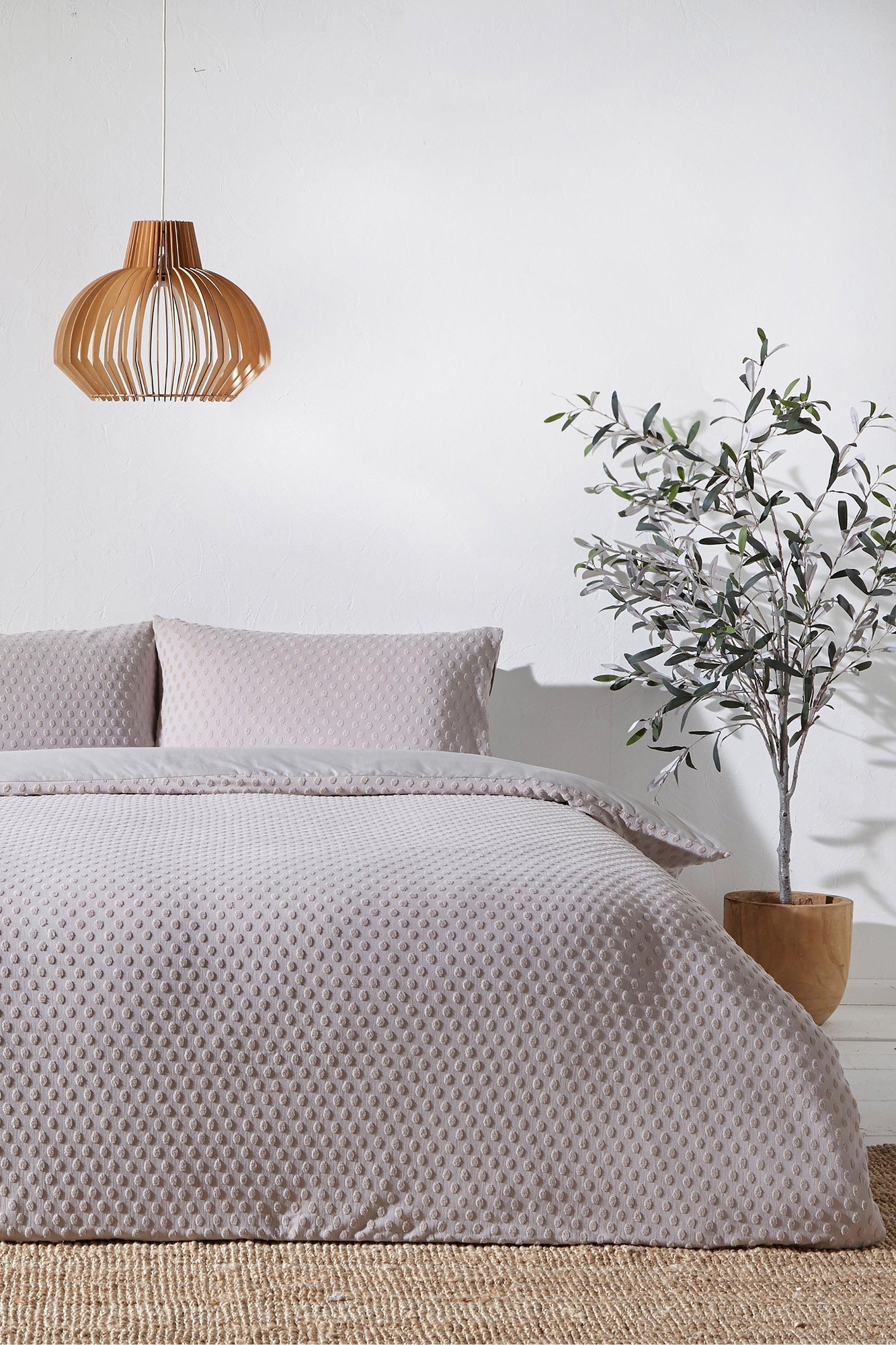 Fluffy stone-colored cotton duvet cover set with polka dots, featuring matching pillowcases, styled with a wooden pendant light and a potted plant.