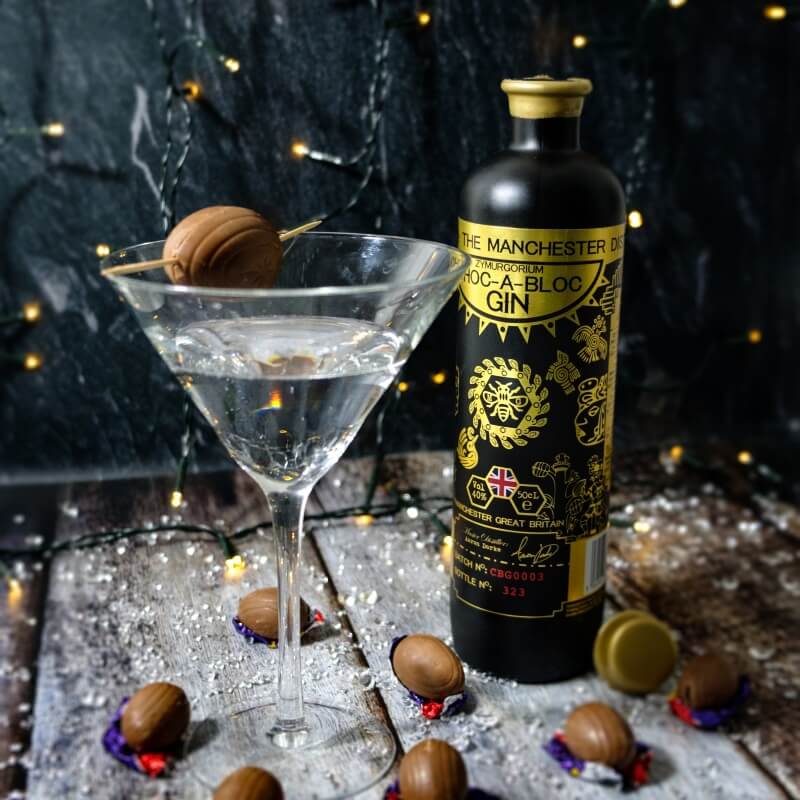 Zymurgorium Choc-O-Bloc Chocolate Flavoured Gin bottle with a black and gold label, beside a martini glass garnished with a chocolate truffle, surrounded by chocolate bonbons.