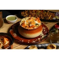 Indian dining set with curry in a clay pot, rice, naan, and drinks on a wooden table.