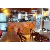 Restaurant interior with wooden tables, red chairs, and a bar with decorative panels, set for a tasting menu experience.