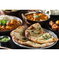Indian meal with naan, curry, rice, and pakoras on a table, featuring vibrant colors and garnished with herbs.