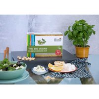 The Big Vegan Cheese Making Kit box with herbs, cheese samples, and a potted basil plant on a table.