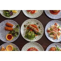 Plates of Italian dishes with greens, meats, and sauces, accompanied by a glass of Prosecco on a dark wooden table.