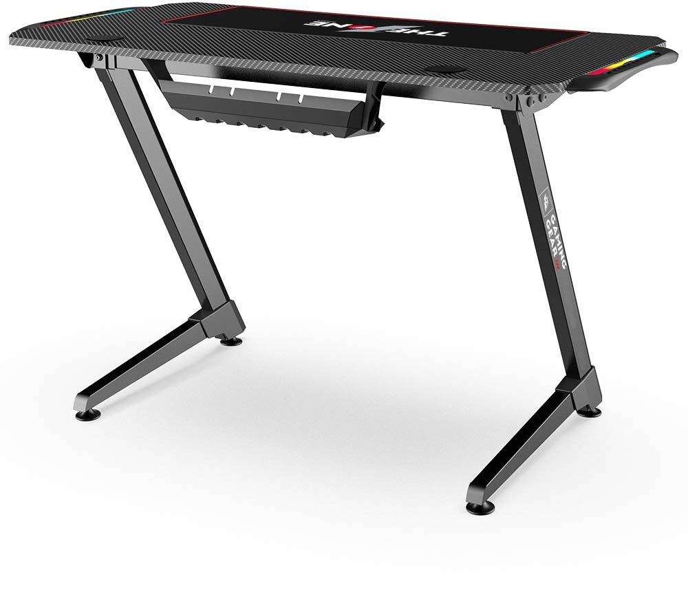 Black and red gaming desk with a carbon fiber texture, featuring a sleek design, cable management tray, and RGB lighting accents on the edges.