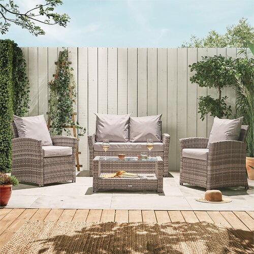Stylish 4-seater garden rattan sofa set in grey, featuring a two-seater sofa, two armchairs, and a glass-top coffee table, complemented by soft cushions and a serene outdoor setting.