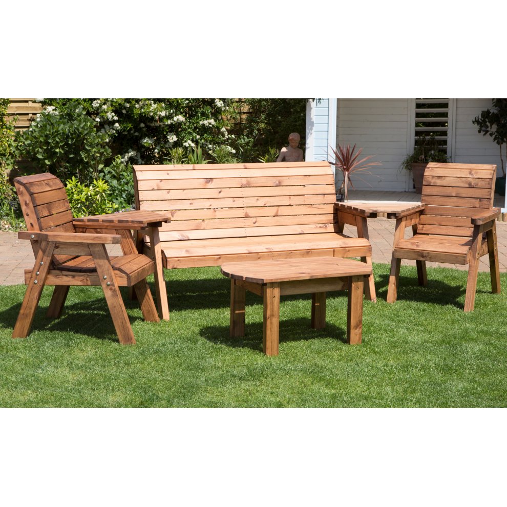 Chunky rustic wooden garden furniture set featuring a 5-seater bench, two armchairs, and a coffee table, all in a warm brown finish, set on green grass.