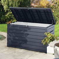 Brown Keter XXL plastic garden storage box, measuring 5' x 3', features a slatted design, a hinged lid, and is set on a patio surrounded by greenery.