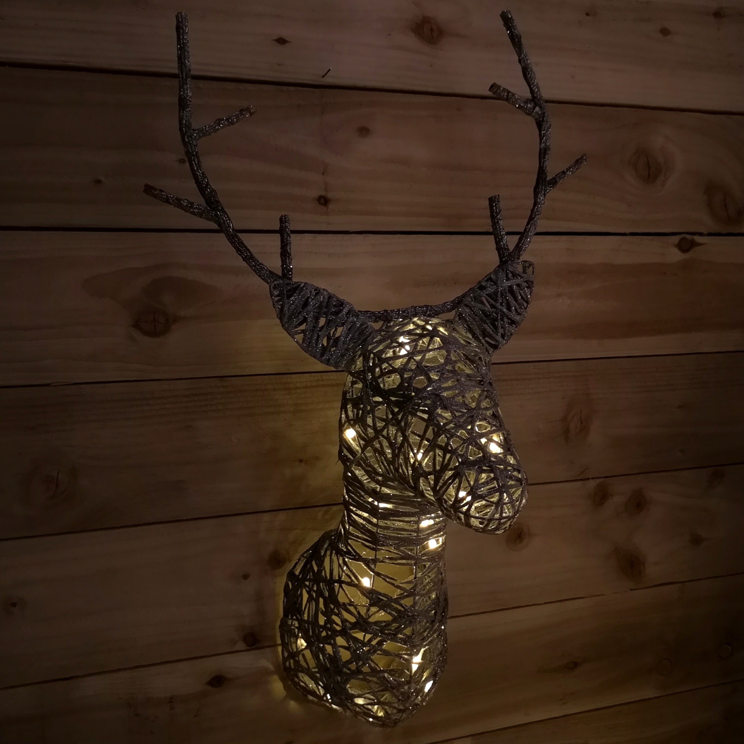 Warm white LED lights illuminate a decorative stag head made of woven twigs, featuring antlers, set against a rustic wooden background.