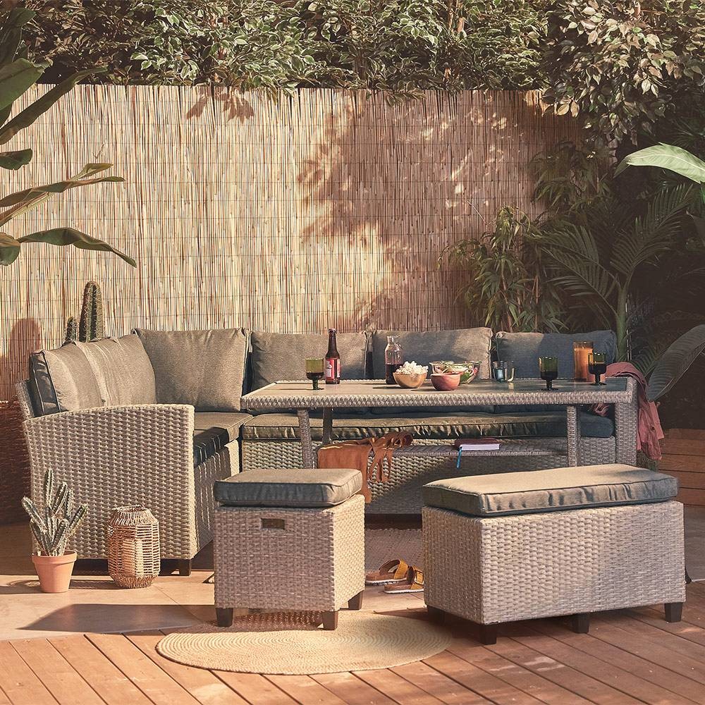 Stylish 9-seater garden rattan corner sofa set in grey with plush cushions, accompanied by a matching dining table, surrounded by greenery and wooden decking.