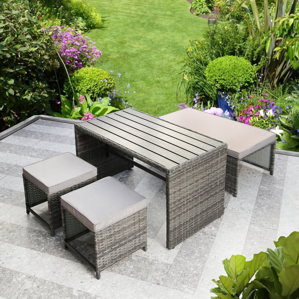 Rattan sofa set featuring a convertible design with a light grey finish, includes two cushioned seats and a rectangular table, set in a lush garden with vibrant flowers.