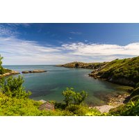 Anglesey coastal view with blue sea, green hills, and clear sky, promoting Trecastell Hotel bed and breakfast stay.
