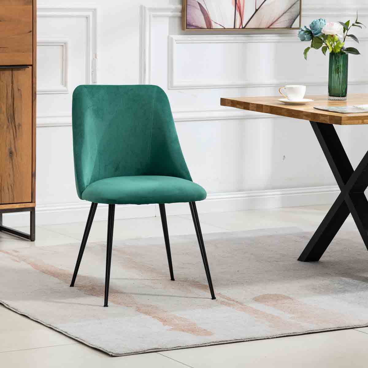 Set of 2 green Morandi velvet dining chairs with sleek black metal legs, positioned beside a wooden table on a light-colored rug in a stylish dining area.