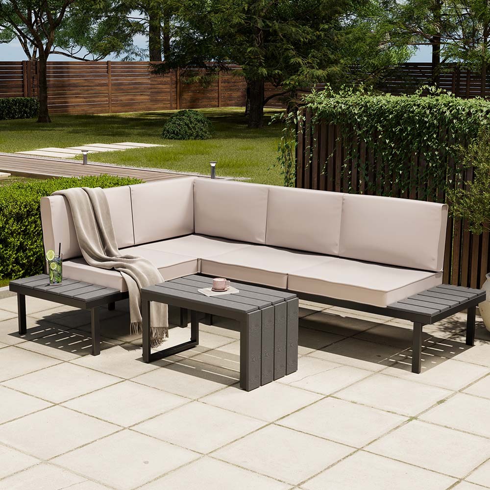 Aruba Modular Garden Furniture Set features a beige cushioned sectional sofa and a matching slatted coffee table, all in a sleek dark frame, set on a patio with greenery in the background.