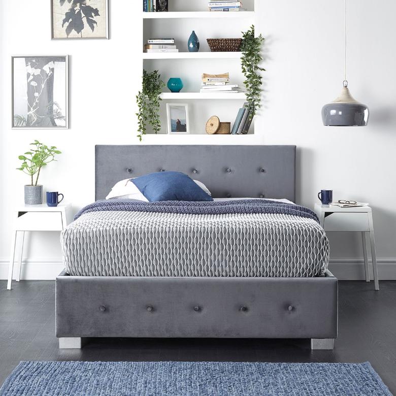 Grey plush velvet king-sized ottoman storage bed with a button-tufted headboard, sleek silver legs, and a cozy blue and white patterned bedding set.