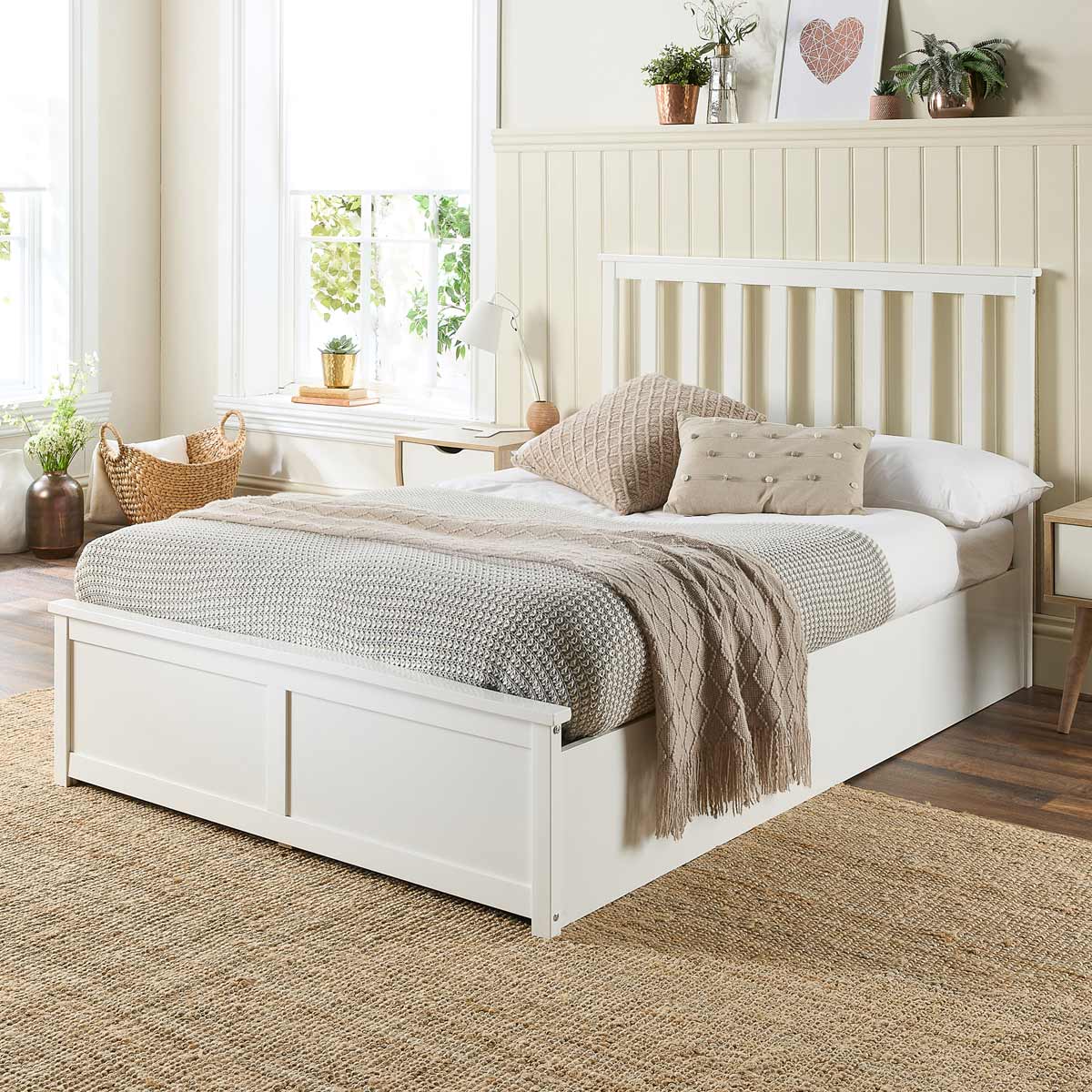 White wooden superking ottoman bed with a slatted headboard, featuring a cozy grey knitted throw and decorative pillows, set in a bright, airy room with natural light.
