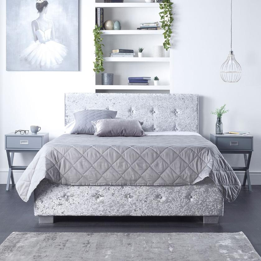 Grey crushed velvet king-size ottoman storage with side opening, featuring a tufted design and sleek silver legs, set against a minimalist bedroom backdrop.