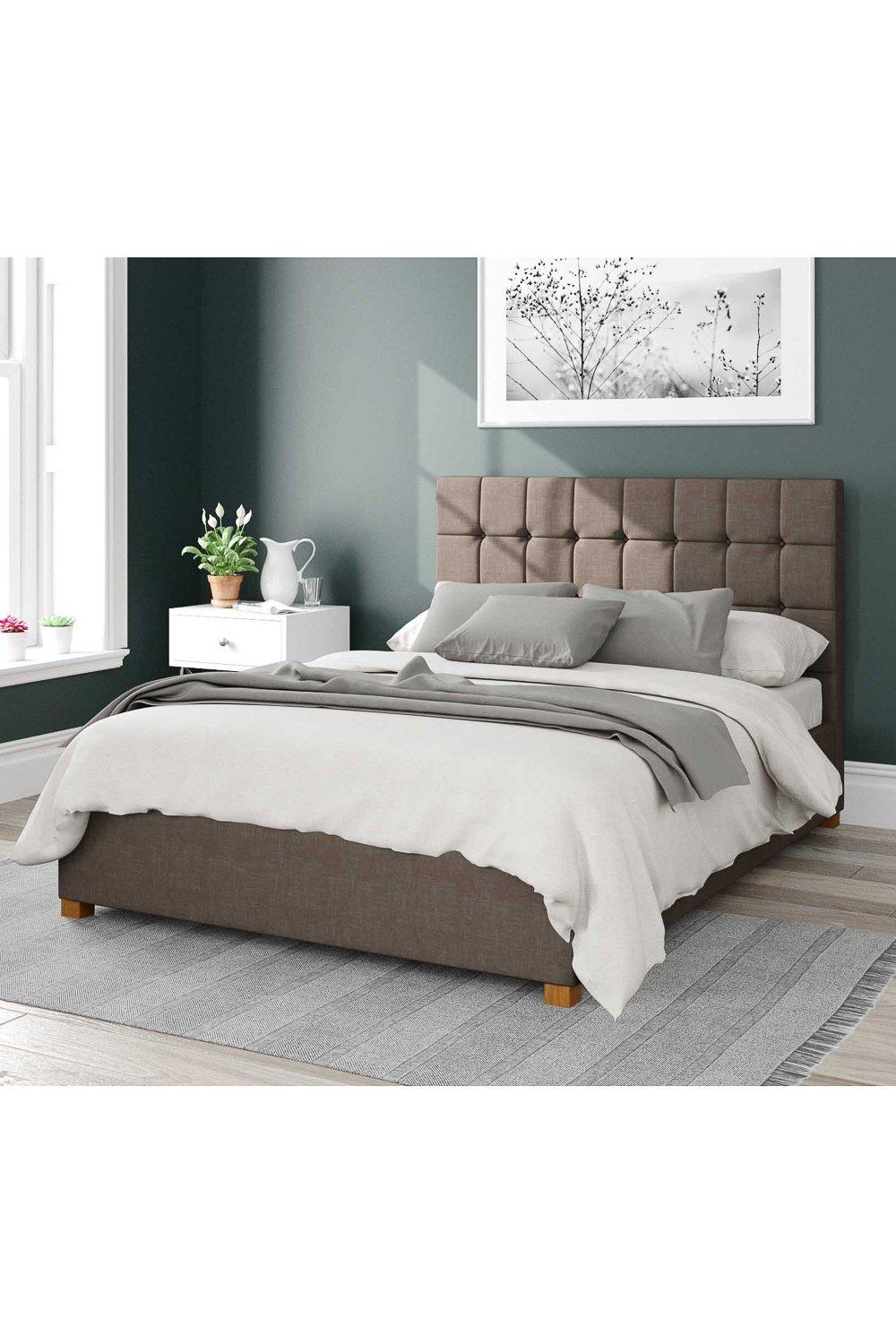 Sinatra Upholstered Ottoman Storage Bed in Malham weave fabric, featuring a tufted headboard, neutral brown color, and wooden legs, with a light gray bedding set on top.