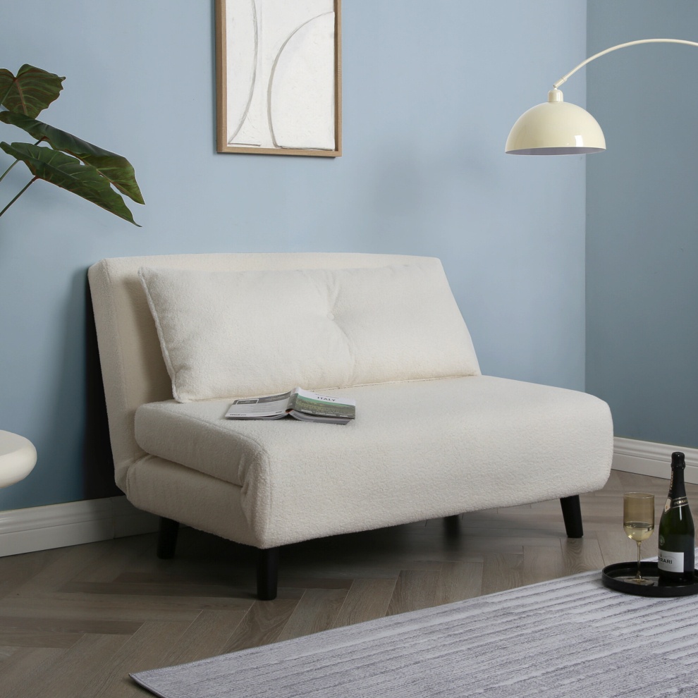 Cream boucle double sofa bed with a minimalist design, featuring two back cushions, black wooden legs, and positioned beside a floor lamp and a small coffee table.