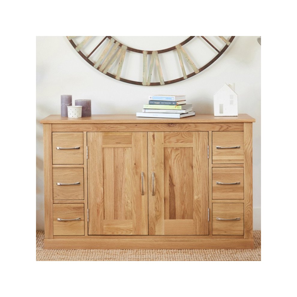 Brown oak six-drawer sideboard featuring a smooth top, two central doors, sleek metal handles, and a natural wood finish, complemented by decorative items and a round mirror.