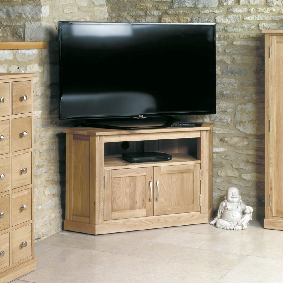 Brown oak corner television cabinet featuring two doors, an open shelf, and a smooth top, set against a stone wall with a large TV and a decorative statue.