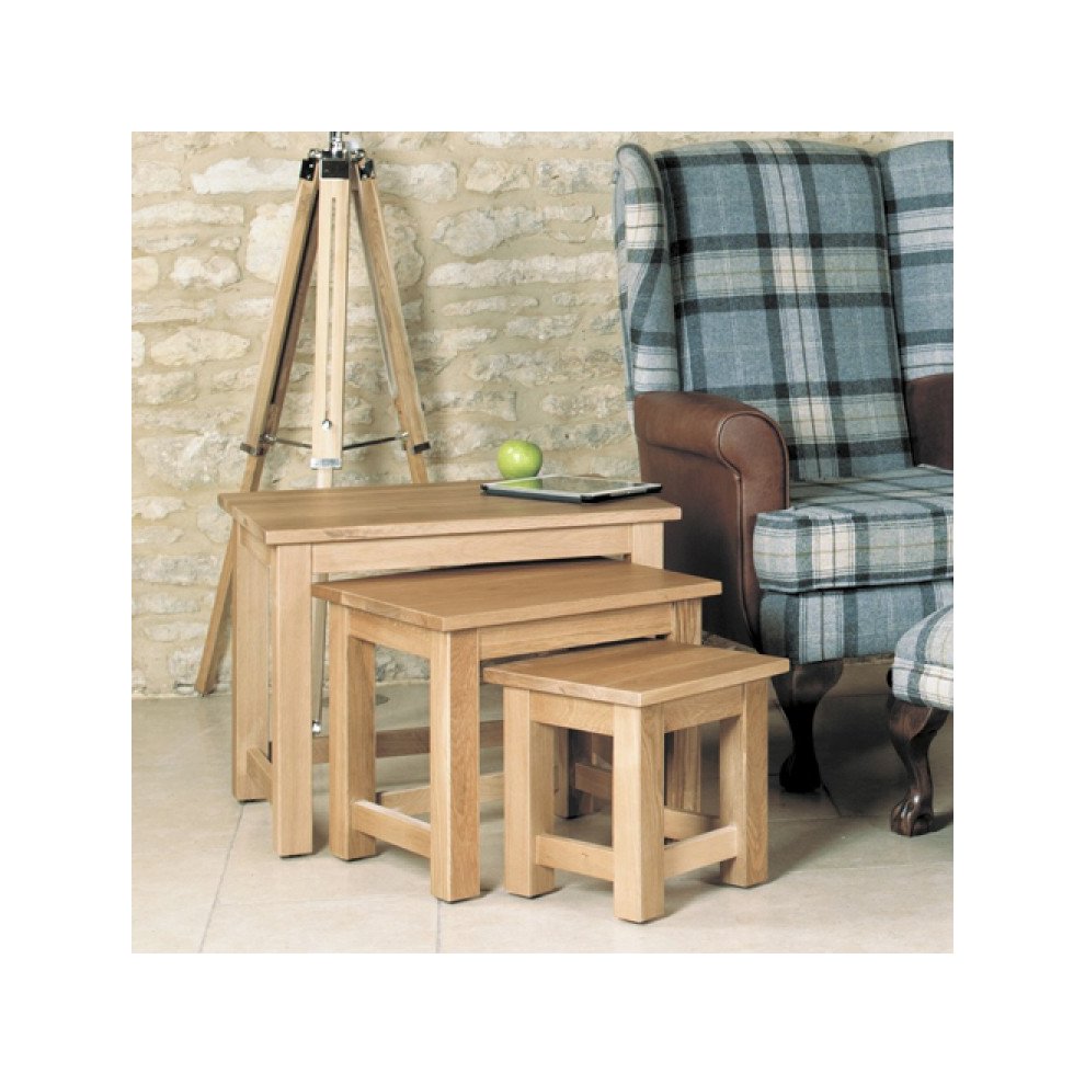 Set of three oak coffee tables in varying sizes, featuring a natural brown finish, sturdy square legs, and a simple design, placed beside a plaid armchair and a decorative tripod.