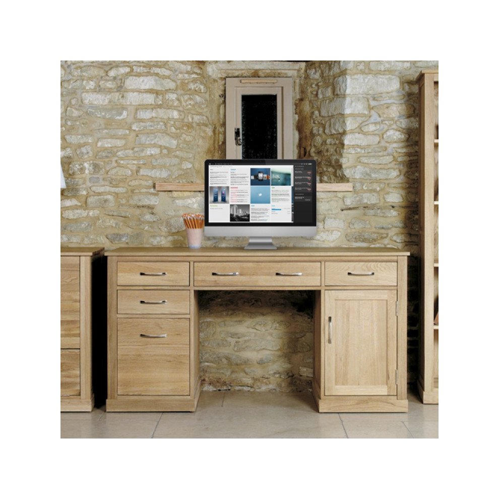 Brown oak twin pedestal computer desk featuring multiple drawers, a cabinet, and a sleek surface, set against a stone wall backdrop with a computer monitor displaying a webpage.