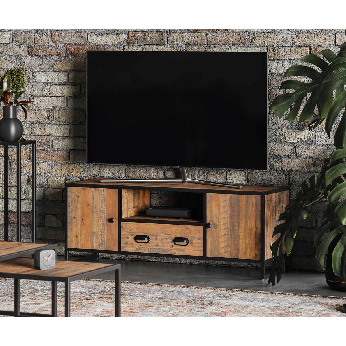 Large brown wooden television cabinet from the Molly and Milo London Rustic Revival Collection, featuring metal accents, two doors, a central shelf, and a sleek design against a brick wall.