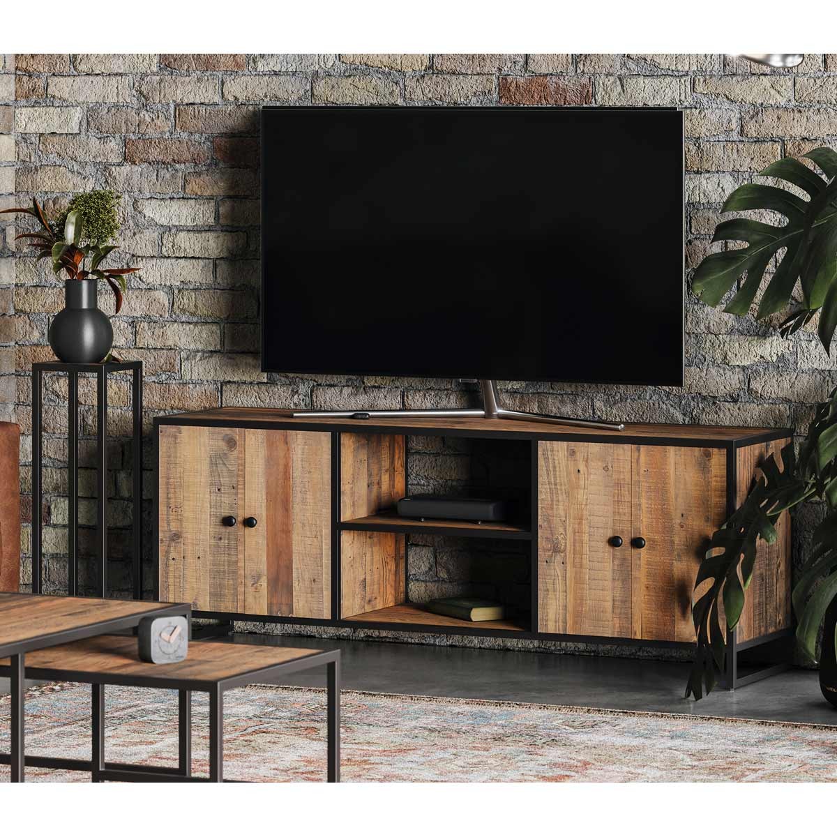 Extra large widescreen television cabinet in brown wood with a rustic finish, featuring two doors, open shelving, and black metal accents, set against a brick wall.