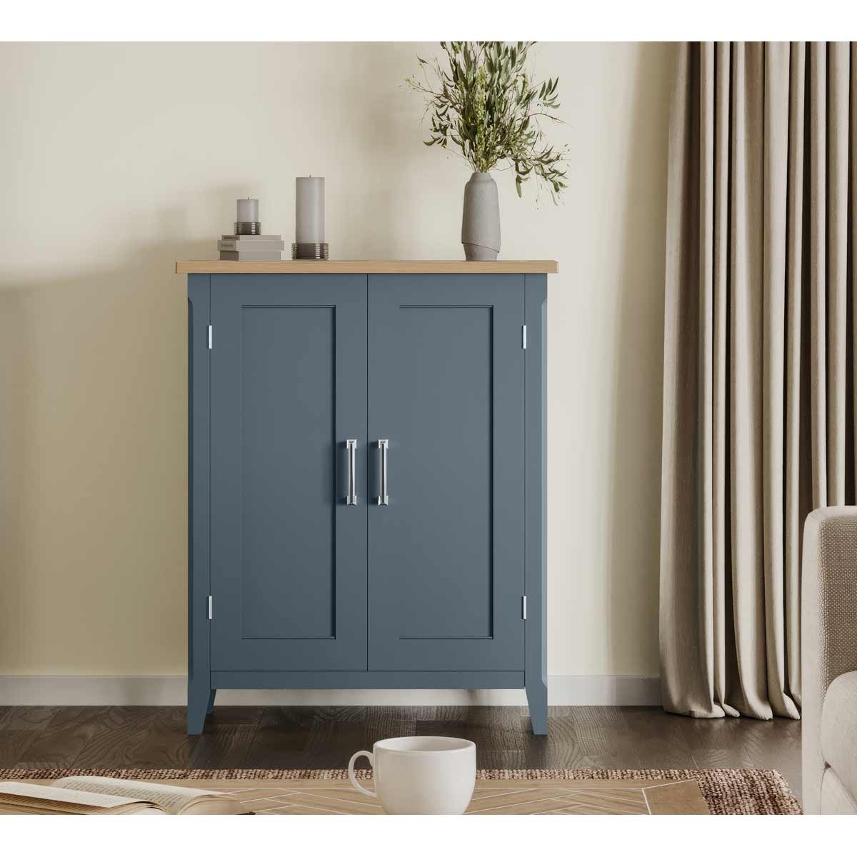 Cobalt blue shoe storage cupboard with a natural wood top, featuring two doors, silver handles, and a sleek design, set against a neutral wall and soft furnishings.