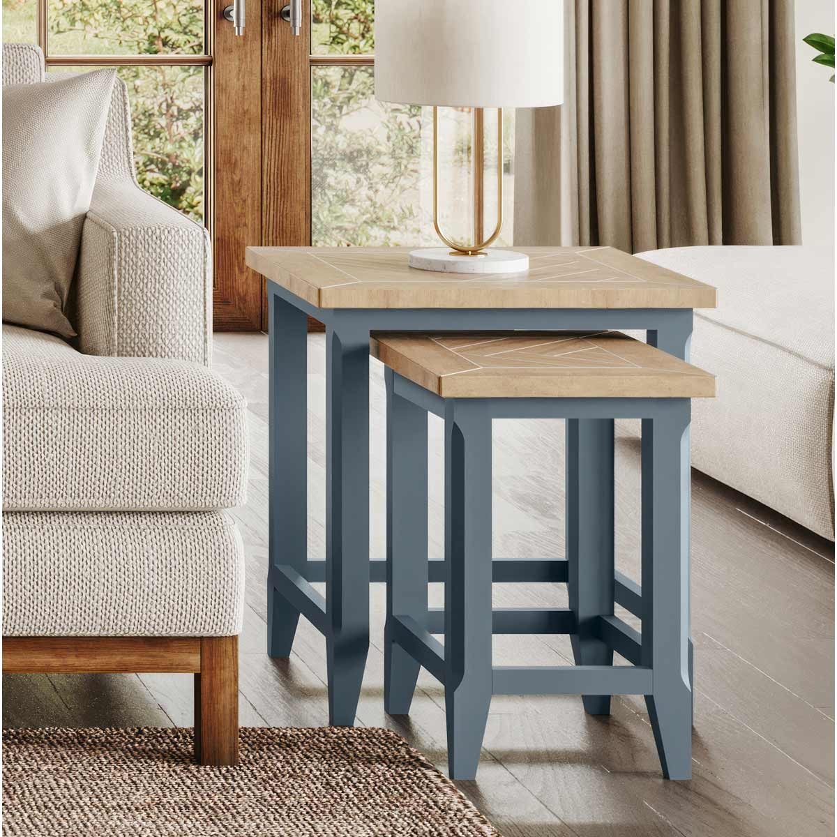 Cobalt blue nest of two tables featuring a natural wood top, geometric design, and sturdy legs, set beside a sofa and lamp in a cozy living space.