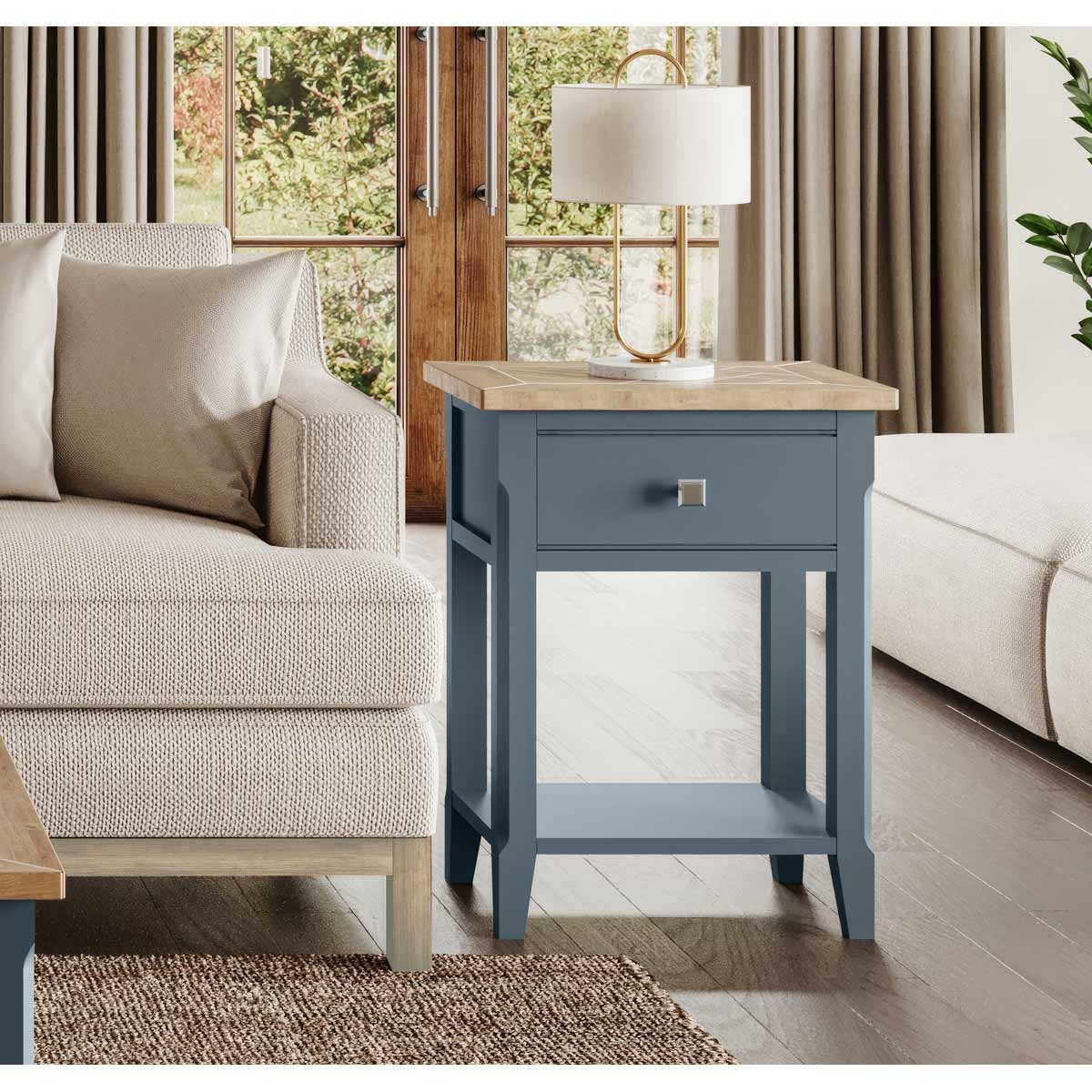 Cobalt blue one-drawer lamp table with a natural wood top, featuring a sleek design and a silver square handle, placed beside a light-colored sofa in a bright living room.