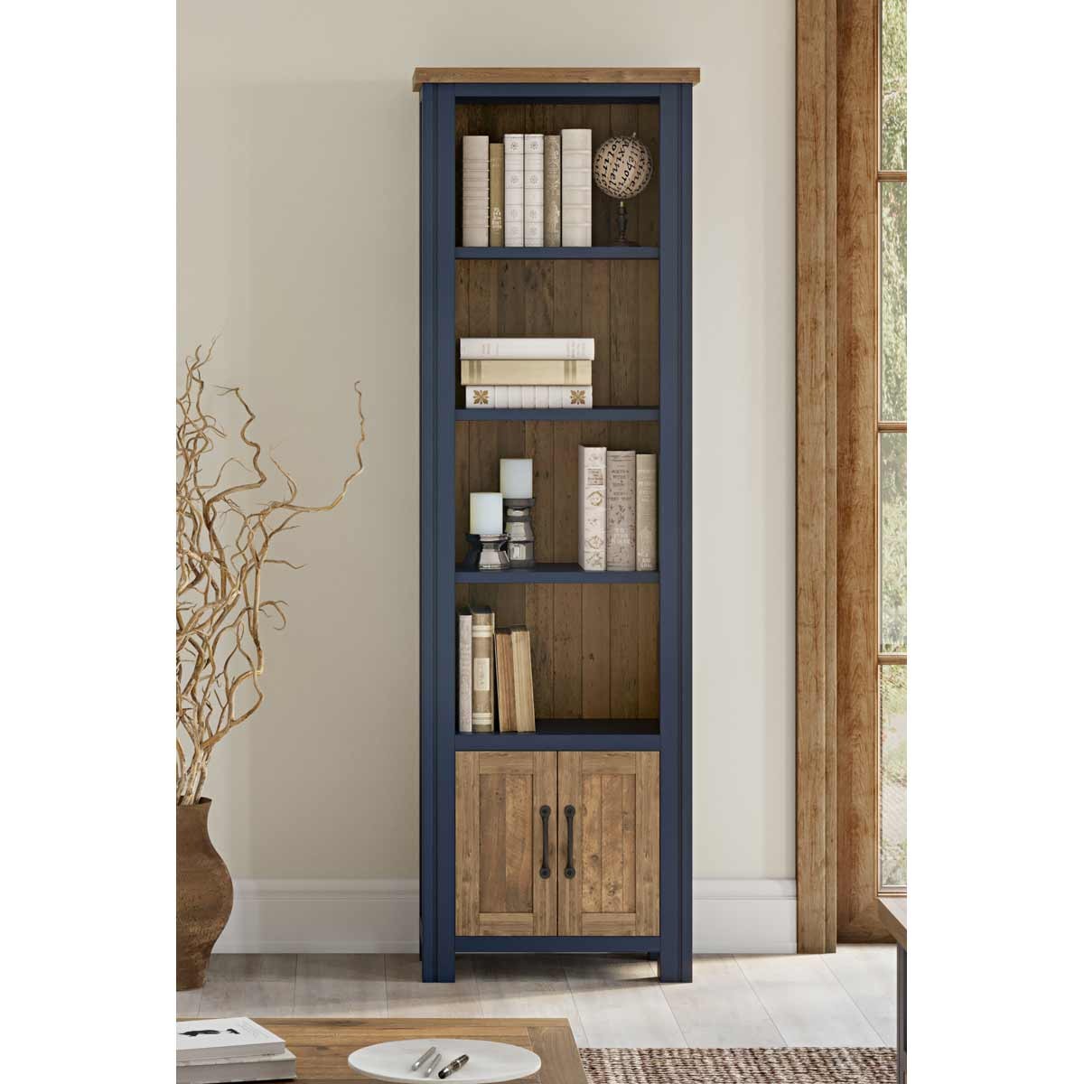 Narrow bookcase in blue with a wooden top, featuring five shelves, two lower cabinets, and decorative items like books and candles displayed.