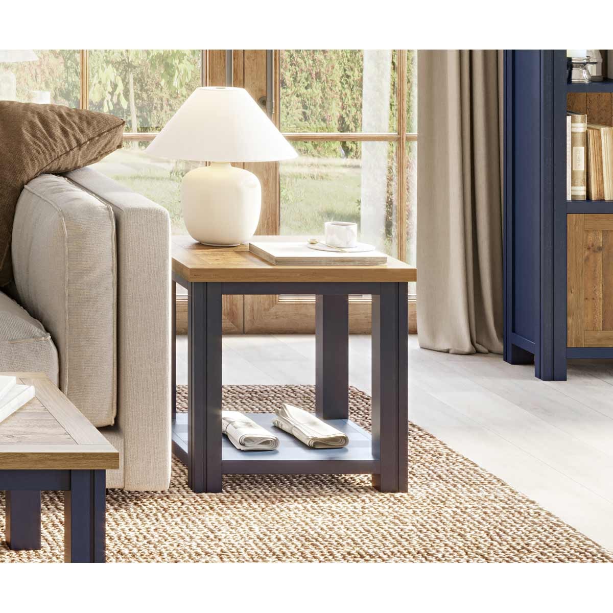 Blue lamp table with a natural wood top, featuring a lower shelf, paired with a white lamp and a cup on top, set beside a light-colored sofa in a bright room.