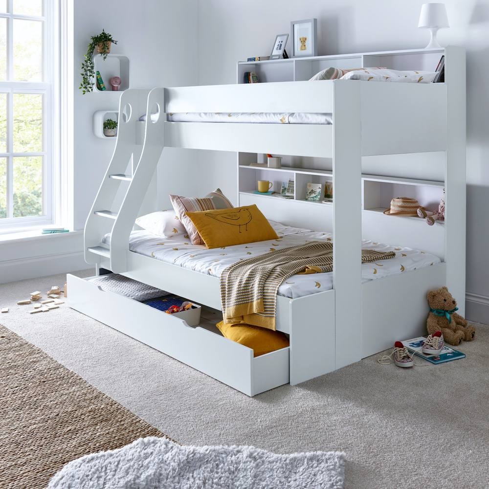 White triple sleeper bunk bed with a small double size, featuring a slide, storage drawer, and two pocket mattresses, set in a bright room with natural light and soft decor.