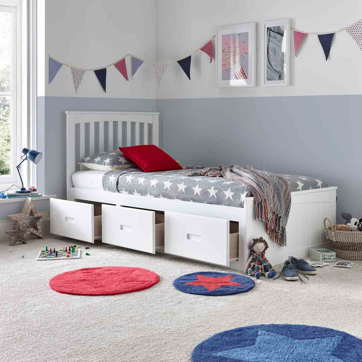White wooden bed with three drawers underneath, paired with a spring mattress featuring a star-patterned gray cover, set in a colorful, child-friendly room.