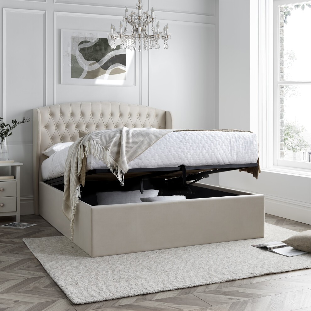Light stone velvet ottoman bed with a tufted headboard, king size, featuring a lift-up mattress for storage, set in a bright room with a chandelier and a textured rug.