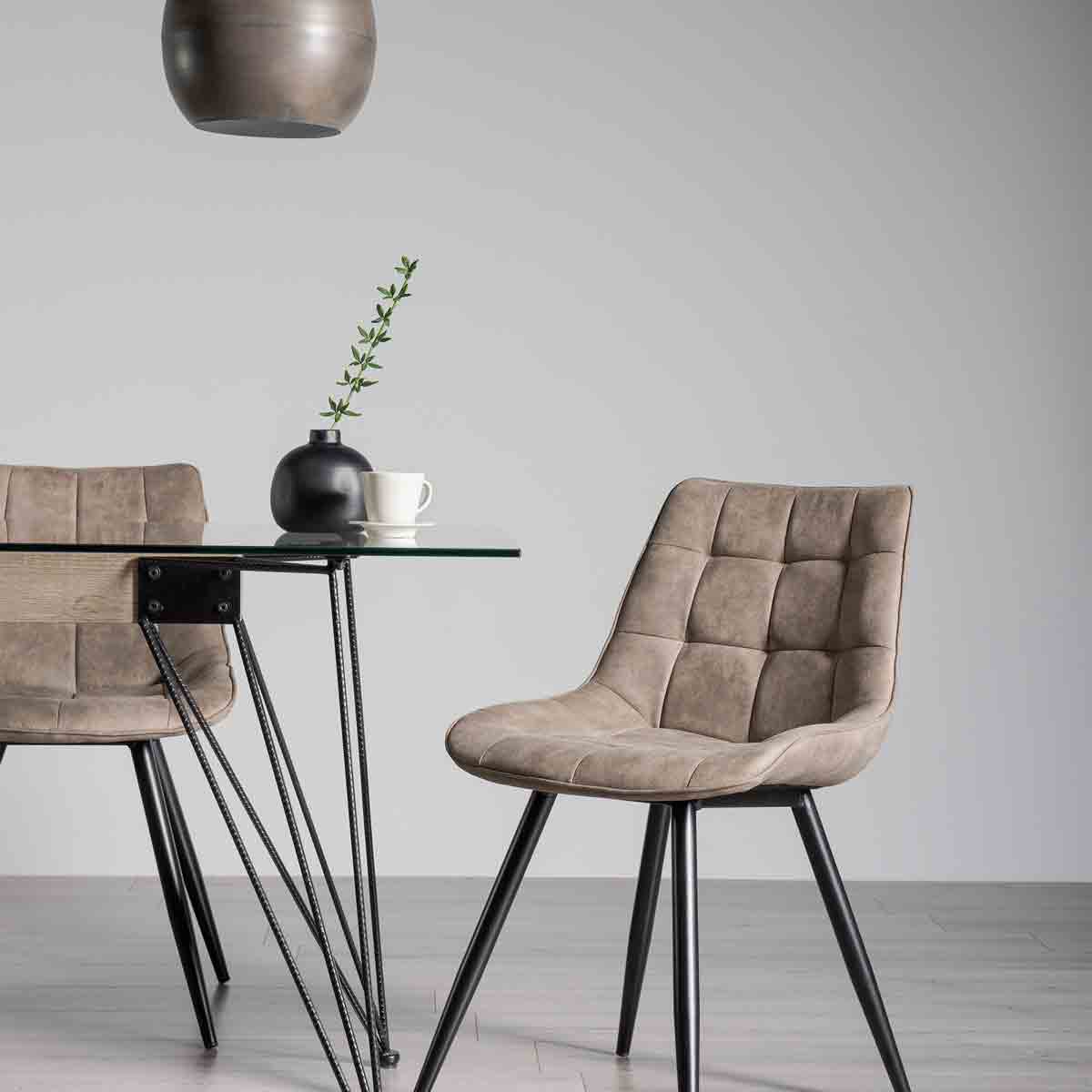 Tan faux suede fabric chairs with a quilted design and black metal legs, positioned next to a glass-top table with a small plant and a cup.