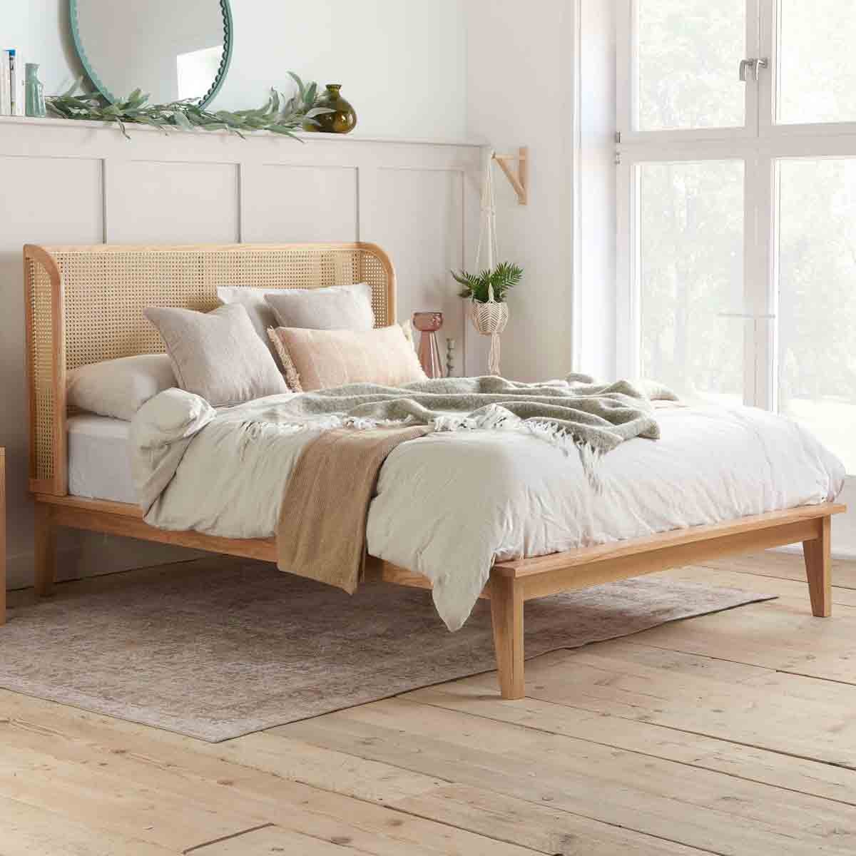 Beige rattan bed frame with a wrap-around design, featuring a wooden base and headboard, complemented by soft bedding and decorative pillows in a light, airy bedroom setting.