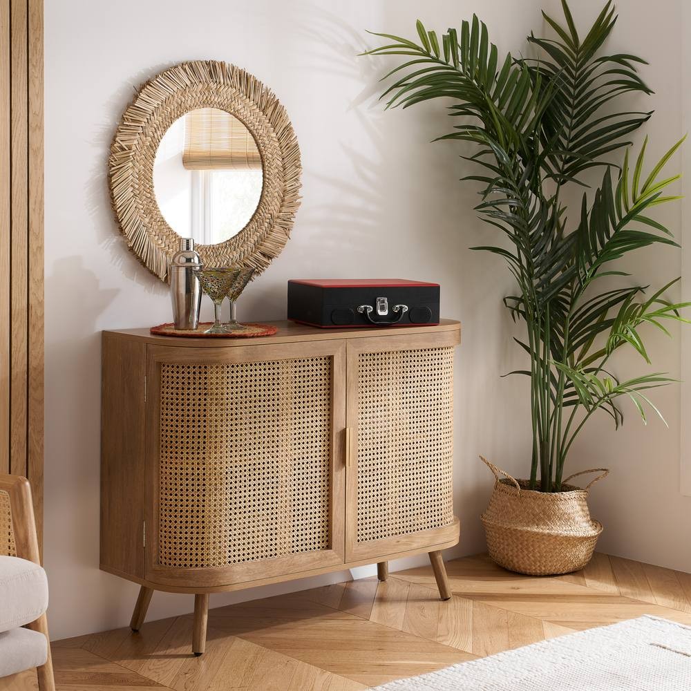 Beige rattan sideboard with curved cupboard design, featuring two doors with woven patterns, wooden legs, and styled with a round mirror and decorative items.