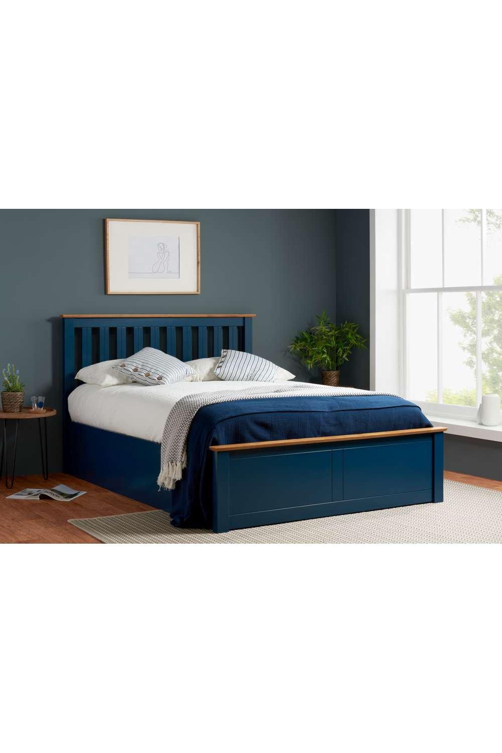 Solid wood ottoman storage bed frame in navy with gas lift mechanism, featuring a slatted headboard, small double size, and a neatly made bed with a blue throw and decorative pillows.
