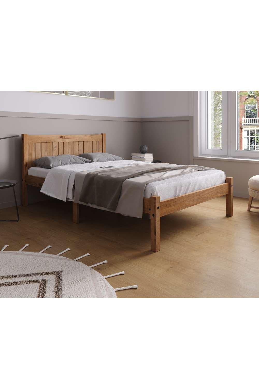 Brown wooden small double bed with a slatted headboard, featuring a low-profile frame and a light grey bedding set, set against a neutral-toned room with natural light.