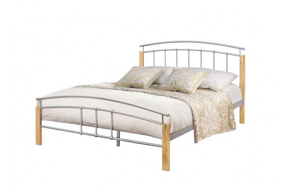 Silver metal bed frame with wooden posts, featuring a curved headboard and footboard, complemented by a light-colored quilt and decorative pillows. Size: Small Double.