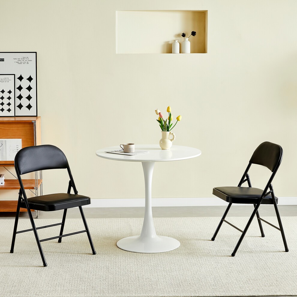 Set of 2 black padded folding chairs with a metal frame, positioned around a white round table, featuring a minimalist design and a small vase of tulips on the table.