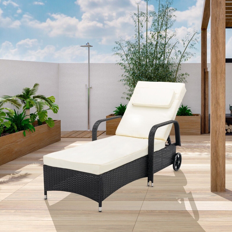 Rattan reclining sun lounger in black with a cream cushion, featuring wheels for mobility, set in a garden with wooden decking and greenery in the background.